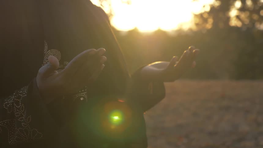 Black woman opens hand and prays outside at sunset