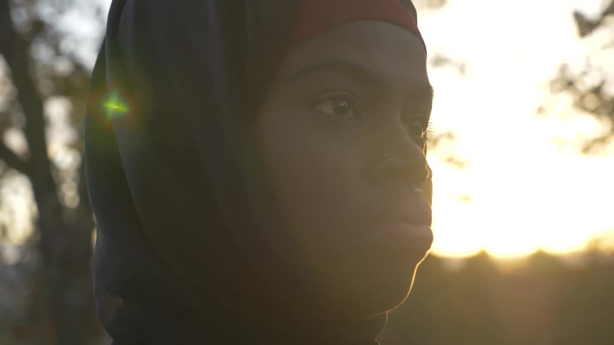 A black woman with a head scarf stares while outdoors