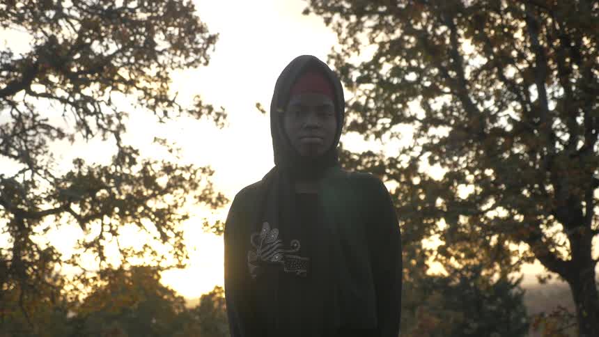 Black girl wearing hoodie looks at the camera outdoors at sunset