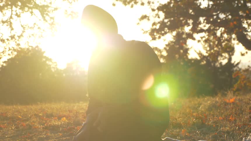A black woman rubs her hand while sitting on a rug outdoors