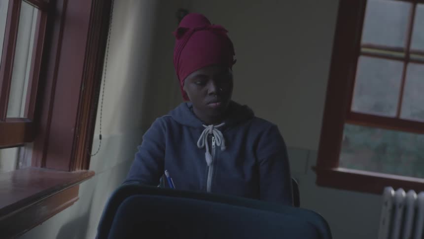 Young black woman wearing head wrap sitting in dark classroom