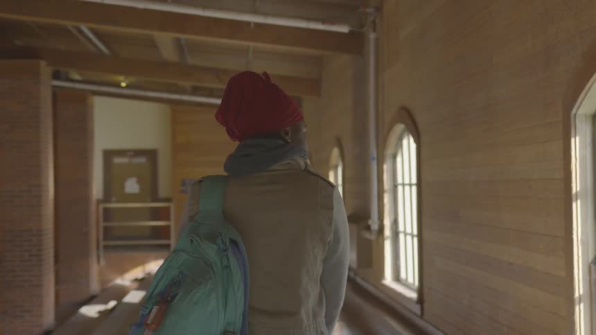 A woman walks down a hallway with a book bag
