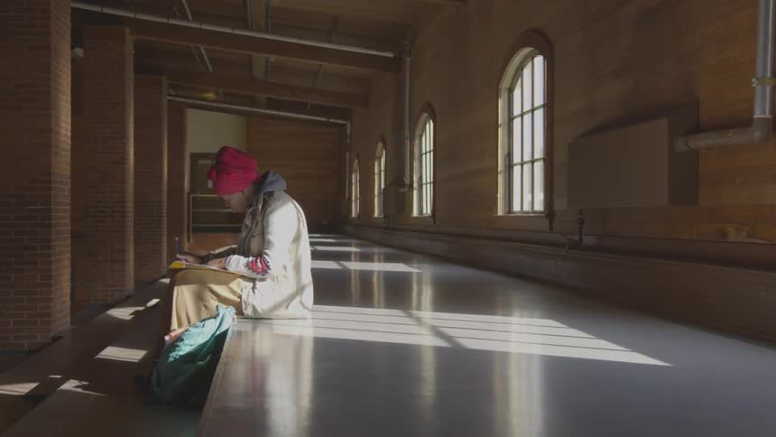 A woman is sitting in the hall writing