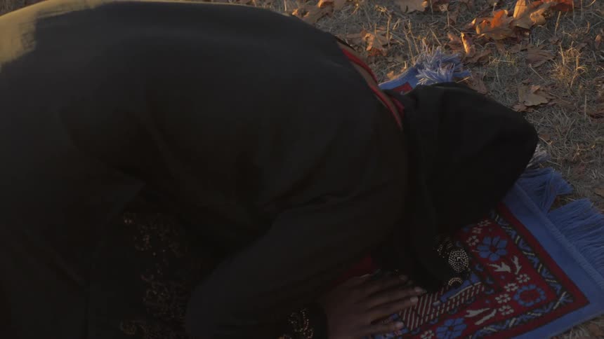 A muslim woman prays on a prayer rug