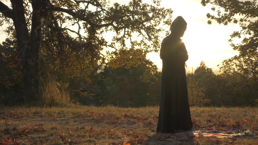 A person wearing a cloak standing in a rural area