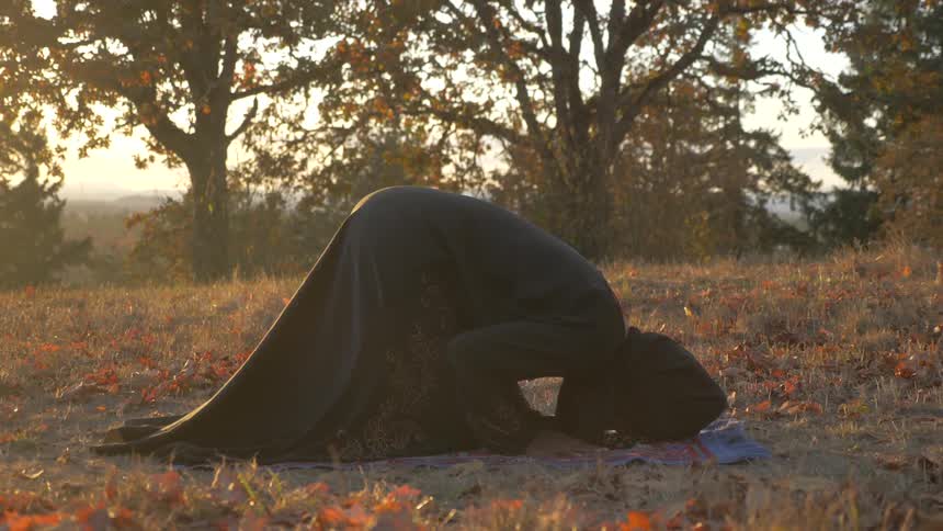 Woman sits on a colorful prayer rug in the grass and prays