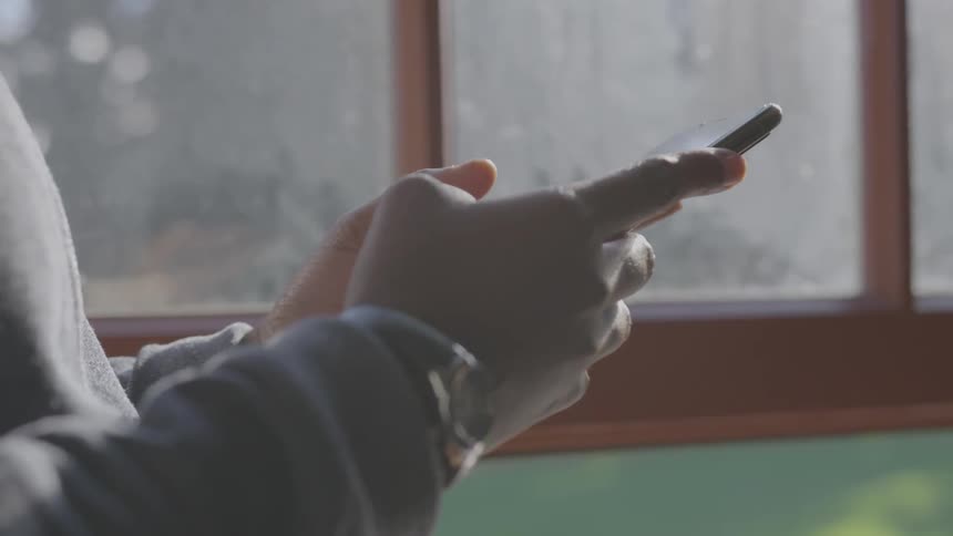 A person standing near a window using a smartphone