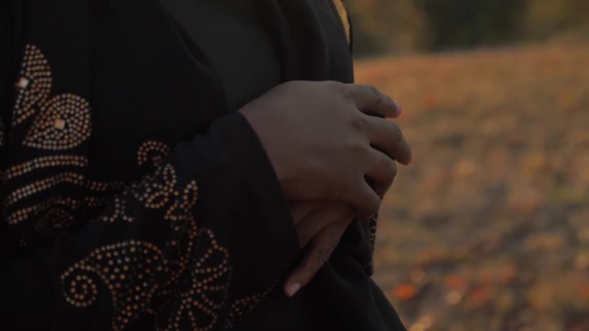 A woman stands outside with her hands clasped over her stomach