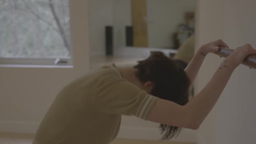 A young woman does knee bends in a dance studio