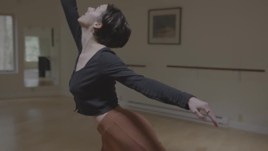 A dancer reaches out with her arm and leg in a dance room