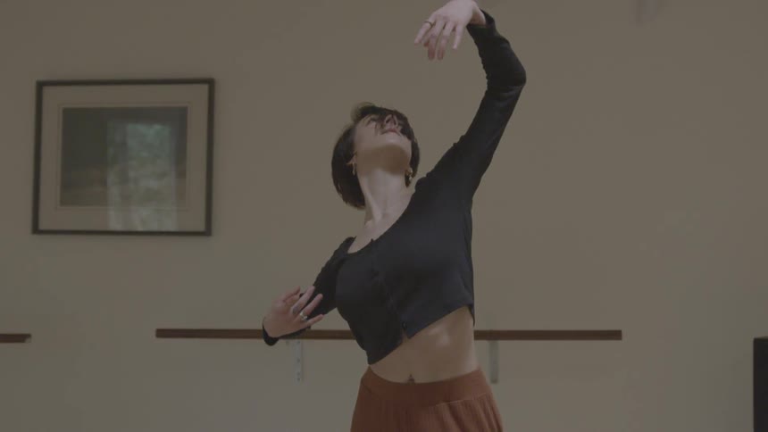 A young woman performing a form of dance in a white walled room