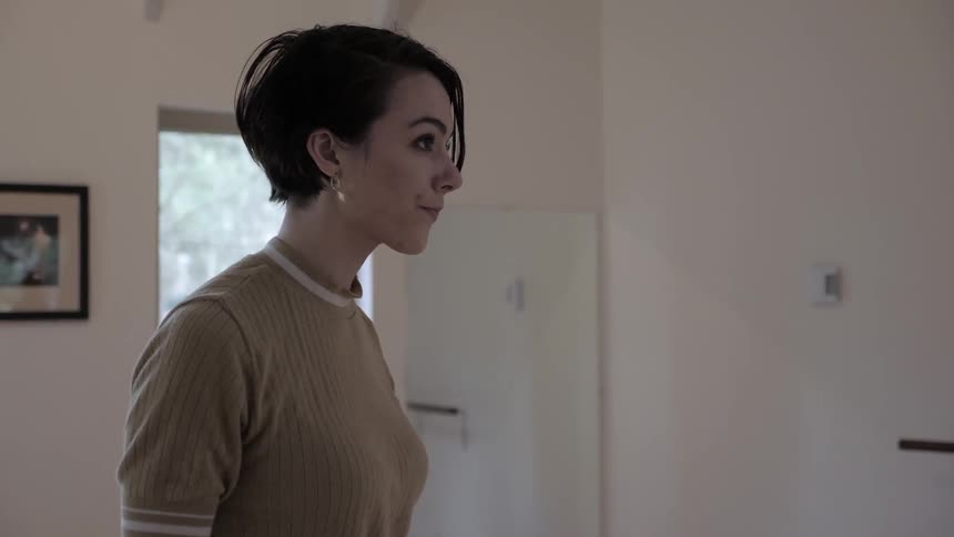 Woman stands and touches hair while looking ahead indoors