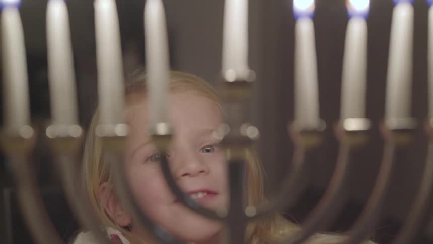 Toddler smiles and looks at burning candles indoors