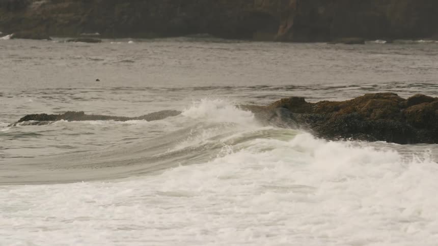 A surfer riding a wave close to an outcropping of rocks
