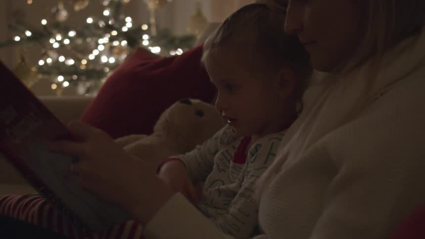 Mother reads book to daughter with christmas tree in the background