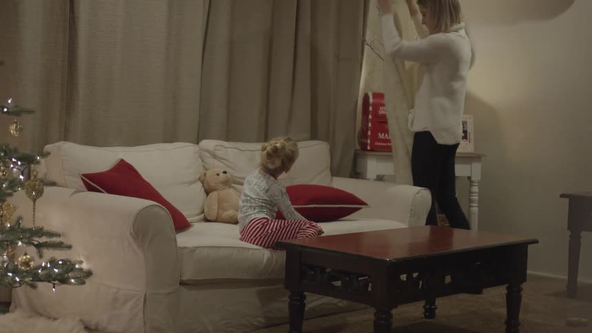 Woman puts blanket on the sofa while the little girl looks at her indoors at night