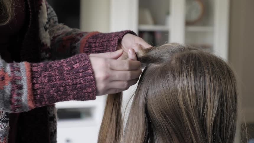 Woman wearing sweater arranges another woman's hair indoors during daylight