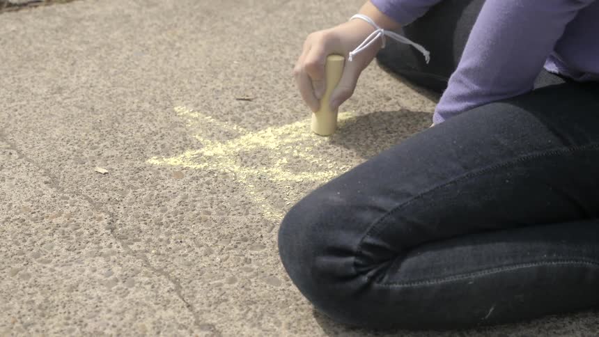 A young girl draws a star on the sidewalk with chalk
