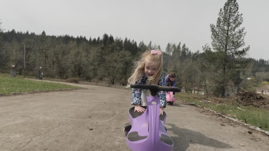 Two girls play on scooters in an empty driveway