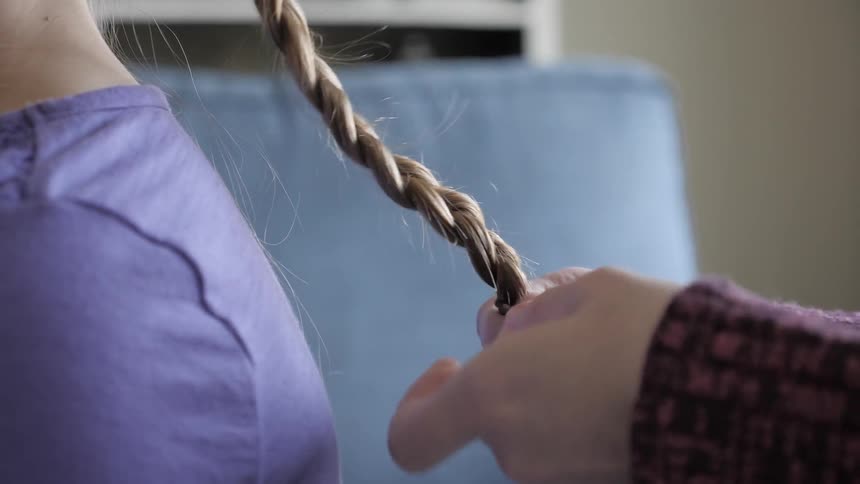 Woman arranges the hair of girl indoors during daylight