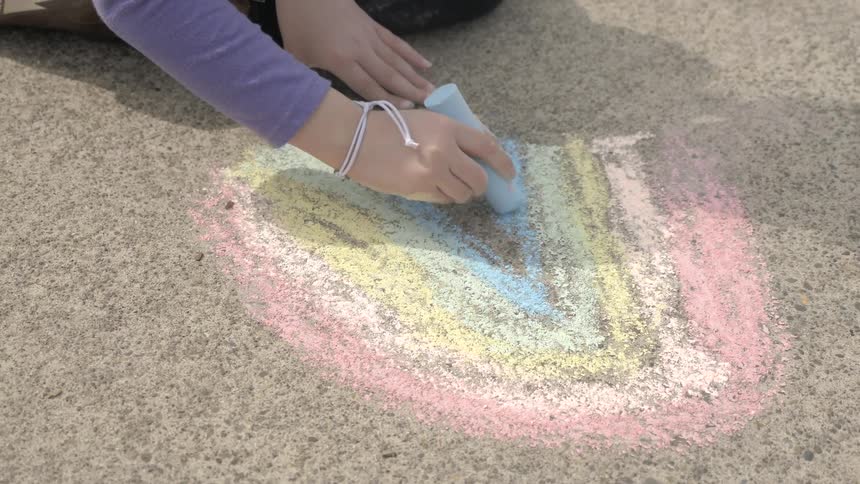 A child makes a chalk rainbow on the concrete