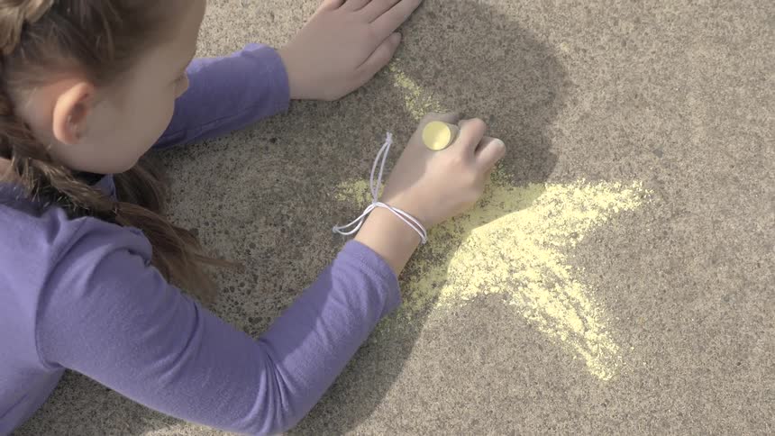 A child draws a star in chalk on a sidewalk