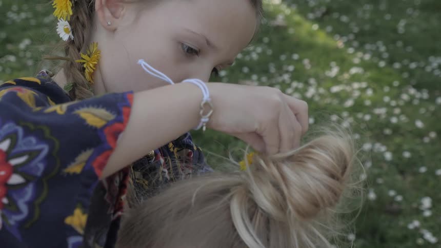 Little girl attaching daisies in a bun on a blonde head