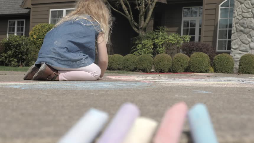 Young girl colors on sidewalk with sidewalk chalk