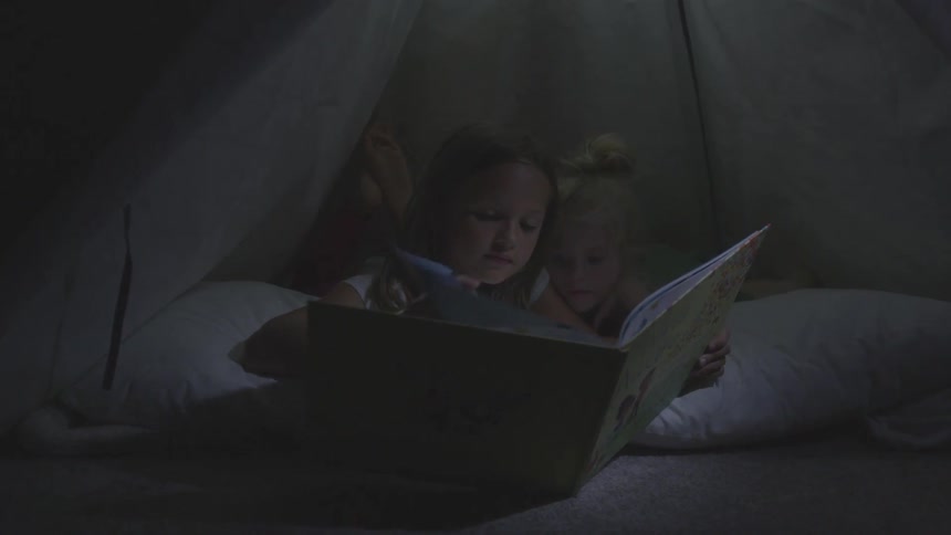 Girls reading a story book on a tent at night