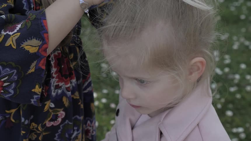 A young girl having a flower tied into her hair by a slightly older girl