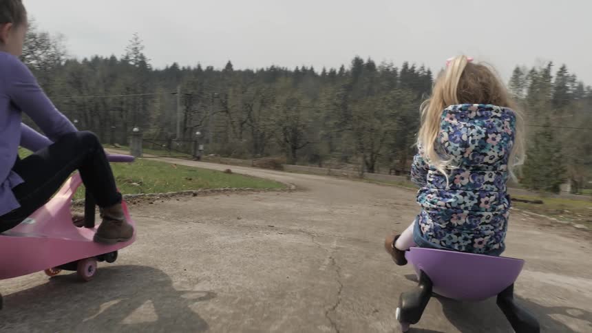 A pair of girls rolling down a hill on plastic carts