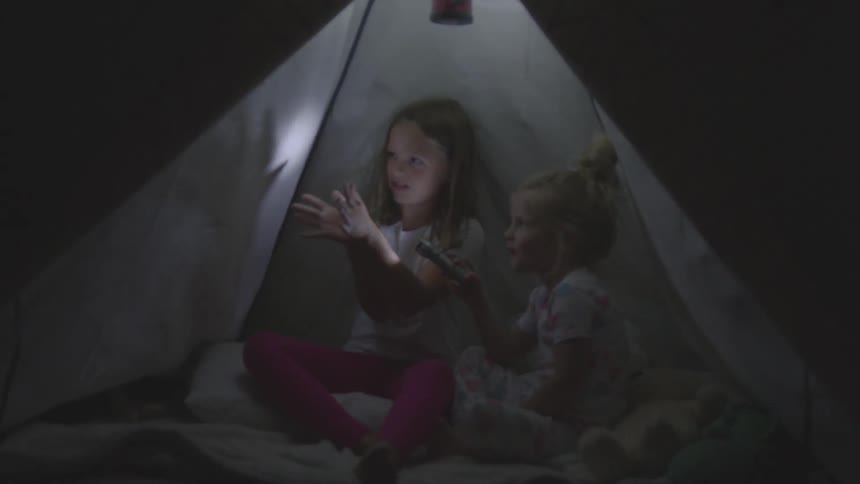 A girl makes shadow puppets with her hands inside a tent for her little sister