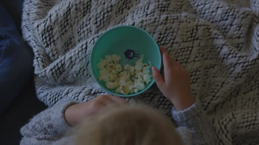Girl under a blanket eating popcorn from a bowl