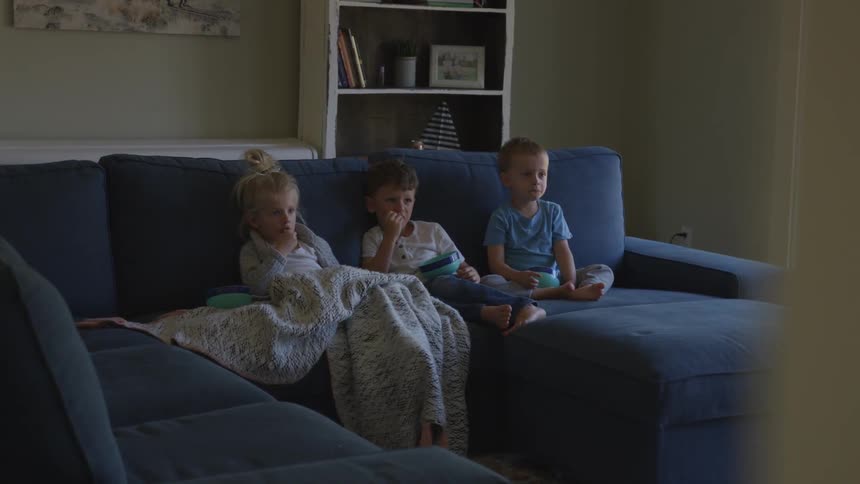 Children sit down on the sofa and watch tv in living room during daylight