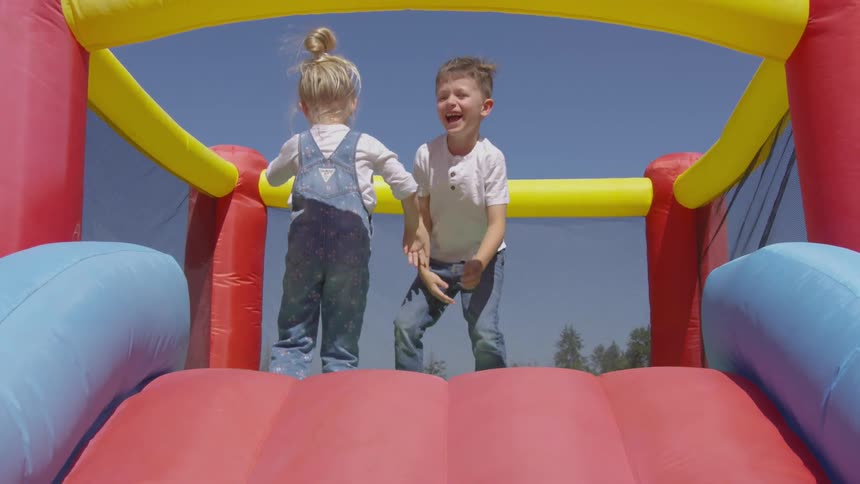 A boy and a girl jump on an inflatable toy while laughing