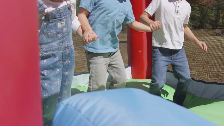 Three children jumping in an outdoors bounce house during the day