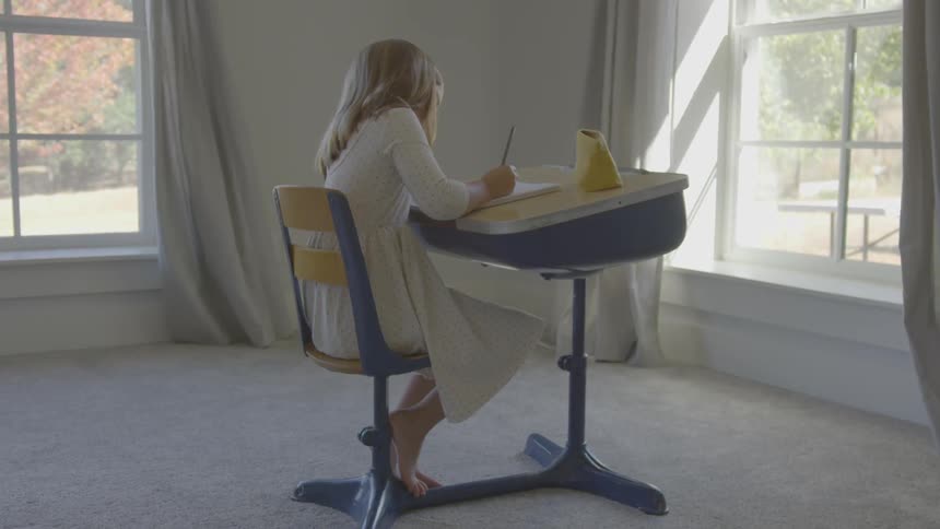 A young girl sits at a desk writing in a notebook
