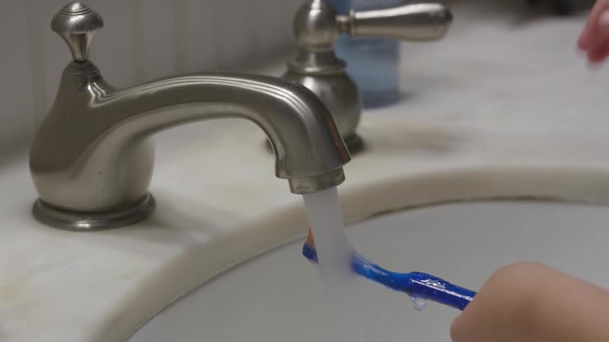 Child wets toothbrush under fountain with water in the bathroom