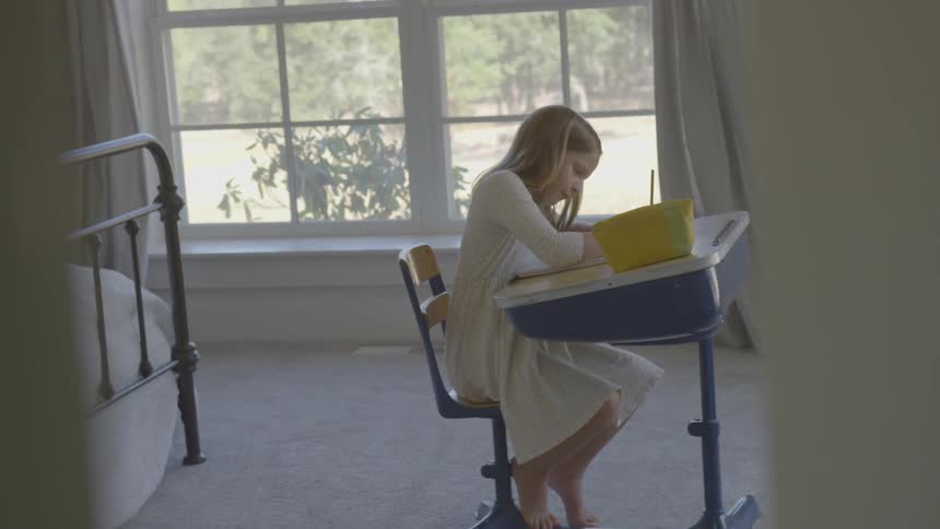 A young girl sits at a desk writing