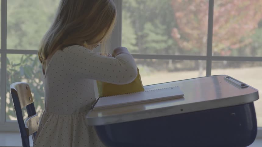 Young girl looks in her pencil case as she sits at a school desk