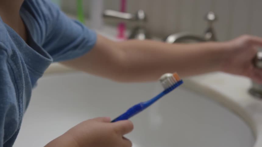A woman puts toothpaste on a toothbrush for a boy