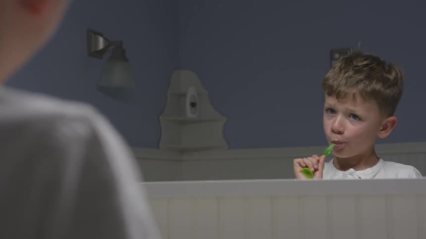 A child brushes their teeth looking the mirror