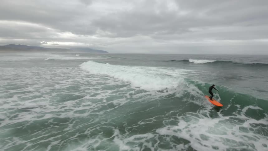 Aerial shot of a surfer riding a wave on a stormy day enjoying life surfing