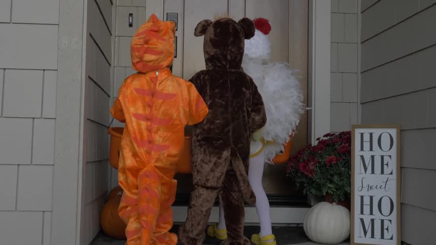 Children in halloween costumes walk up to a front door while trick or treating