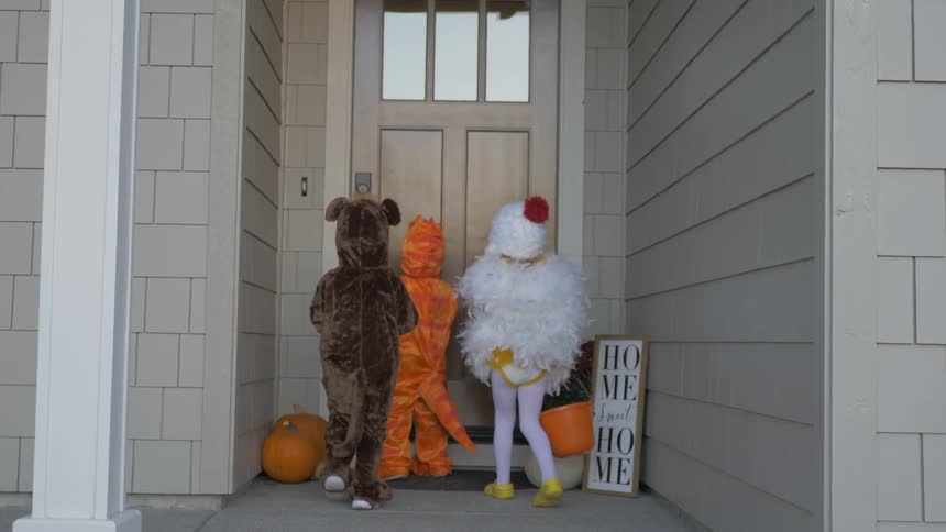 Children in costumes walk up to a front door while trick or treating
