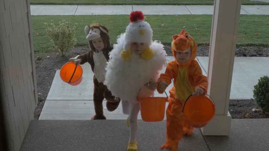 Children dressed up in costumes approach a front door while trick or treating