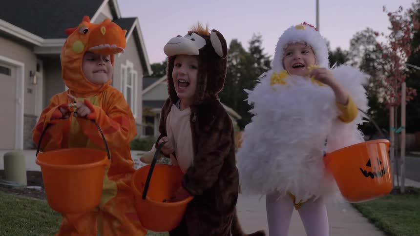 Children wearing halloween costume dances on the pavement in the neighborhood at dusk
