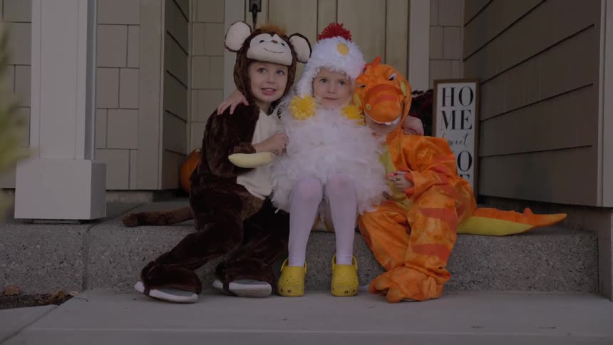 Three children in costumes sit on a front step