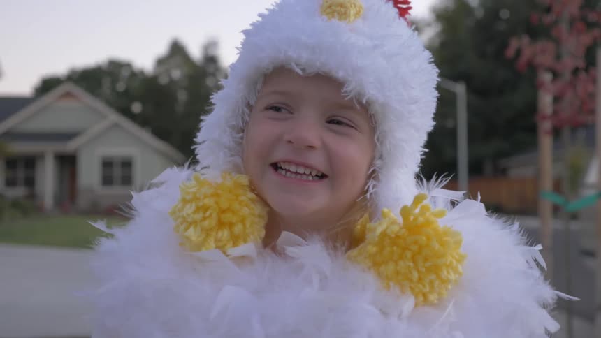 Girl wearing chicken costume laughs in the neighborhood at dusk