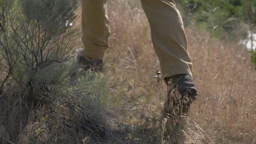 A hiker is walking on a narrow path wearing hiking boots and using hiking poles